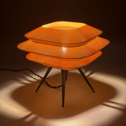 BLOC Caramel lit on a pale surface, three stacked knit-textured tiers glowing warm above black tripod legs