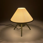 MILLINER Matcha lit on a pale surface, its wide woven brim glowing above three slim matcha-green legs
