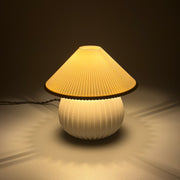 MIRO Ivory lit on a soft pale surface, its pleated shade casting a scalloped ring of warm light