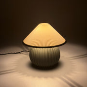 MIRO Olive lit on a soft pale surface, its pleated shade casting a scalloped ring of warm light